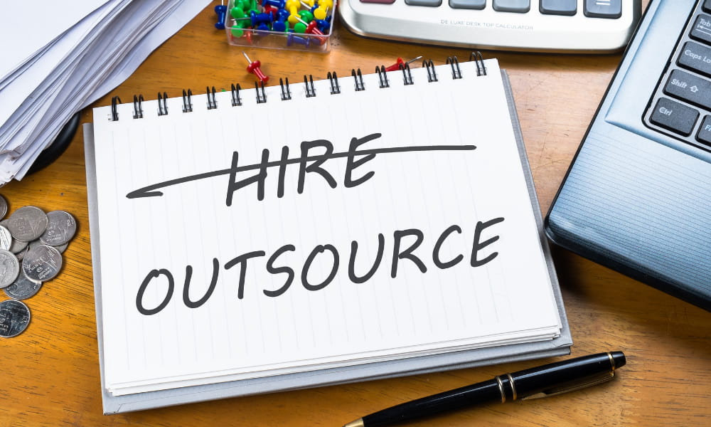 The word hire crossed out on paper and outsource written